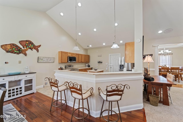 kitchen featuring a kitchen bar, dark wood-type flooring, stainless steel appliances, a peninsula, and light countertops