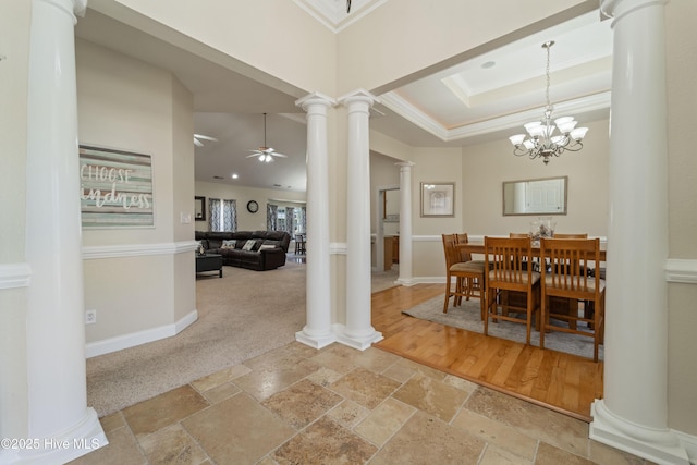 dining area with ornate columns, stone tile flooring, ornamental molding, a raised ceiling, and ceiling fan with notable chandelier