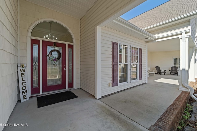 entrance to property with a porch and a shingled roof