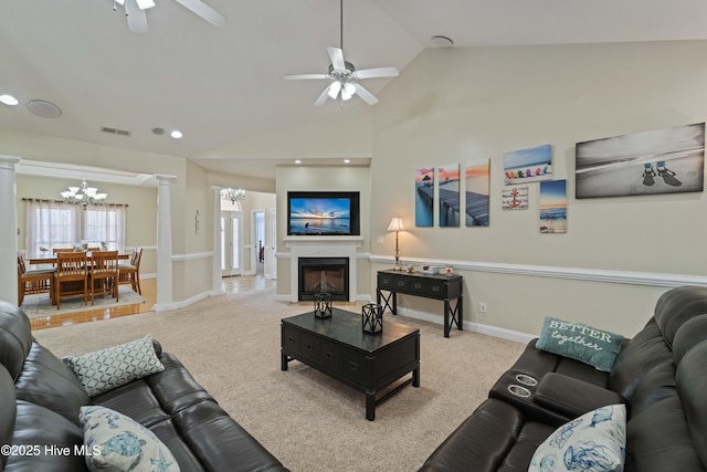 carpeted living area with visible vents, ceiling fan with notable chandelier, ornate columns, a fireplace, and vaulted ceiling