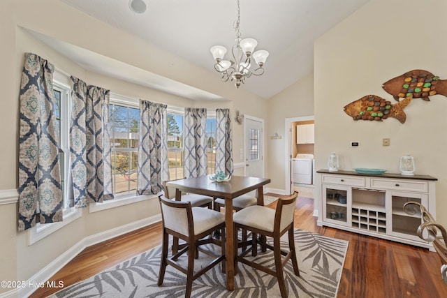 dining space featuring a notable chandelier, lofted ceiling, wood finished floors, baseboards, and washer / dryer