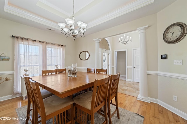 dining area with ornate columns, an inviting chandelier, crown molding, light wood-style floors, and a raised ceiling