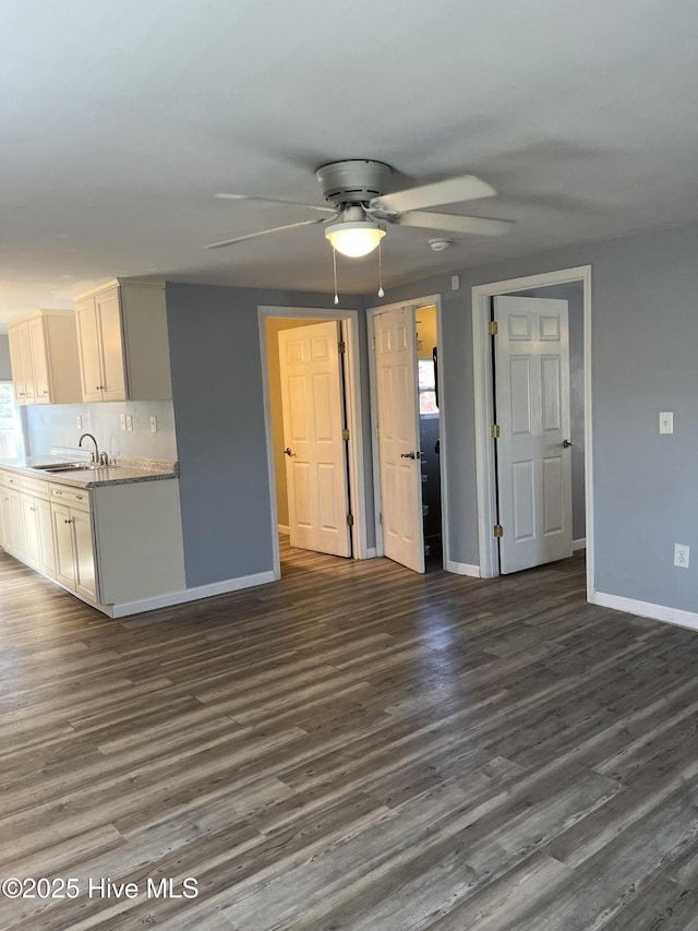 unfurnished living room featuring dark wood-style floors, baseboards, ceiling fan, and a sink