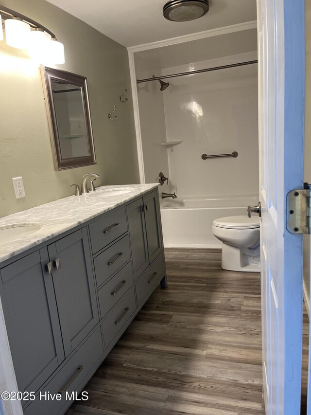 bathroom featuring wood finished floors, double vanity, a sink, toilet, and shower / bathtub combination
