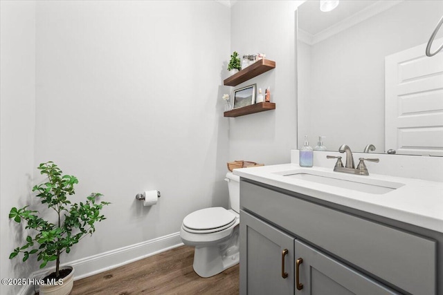 bathroom with toilet, wood finished floors, vanity, baseboards, and crown molding