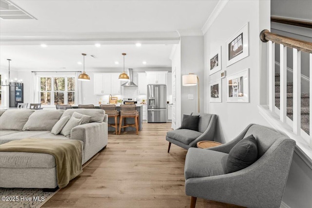 living room featuring visible vents, stairway, crown molding, light wood-type flooring, and a chandelier