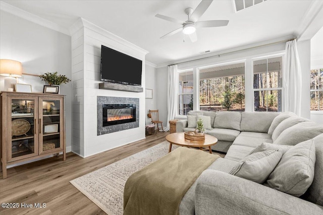 living area with visible vents, ornamental molding, a glass covered fireplace, ceiling fan, and wood finished floors