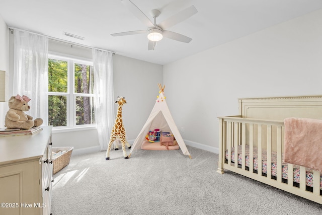 carpeted bedroom with ceiling fan, a crib, visible vents, and baseboards