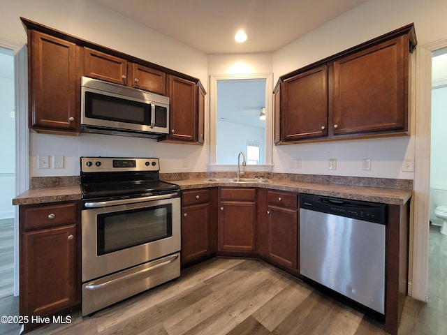 kitchen featuring dark countertops, light wood-type flooring, appliances with stainless steel finishes, and a sink