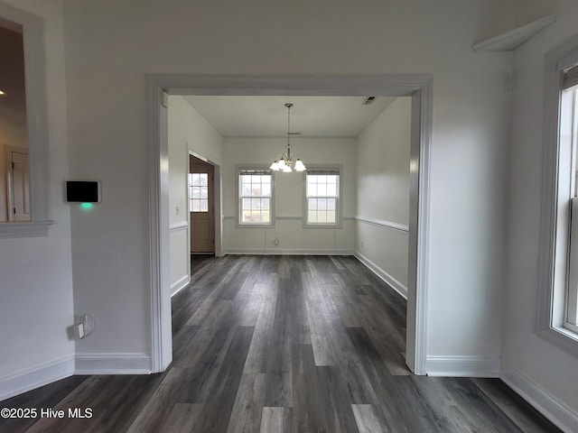 unfurnished dining area featuring baseboards, dark wood-type flooring, and a chandelier