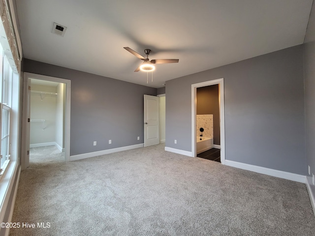 unfurnished bedroom featuring visible vents, ensuite bath, dark carpet, baseboards, and a spacious closet