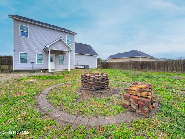 back of house featuring central AC unit, an outdoor fire pit, a lawn, and a fenced backyard