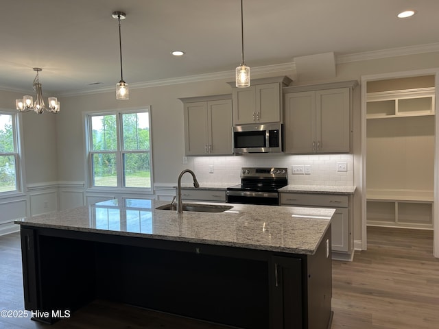 kitchen featuring appliances with stainless steel finishes, a sink, decorative backsplash, light stone counters, and ornamental molding