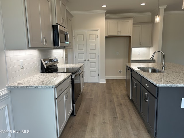 kitchen featuring appliances with stainless steel finishes, a sink, ornamental molding, light stone countertops, and wood finished floors