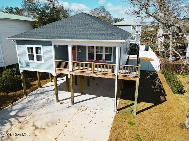 back of property with concrete driveway, a carport, roof with shingles, and fence