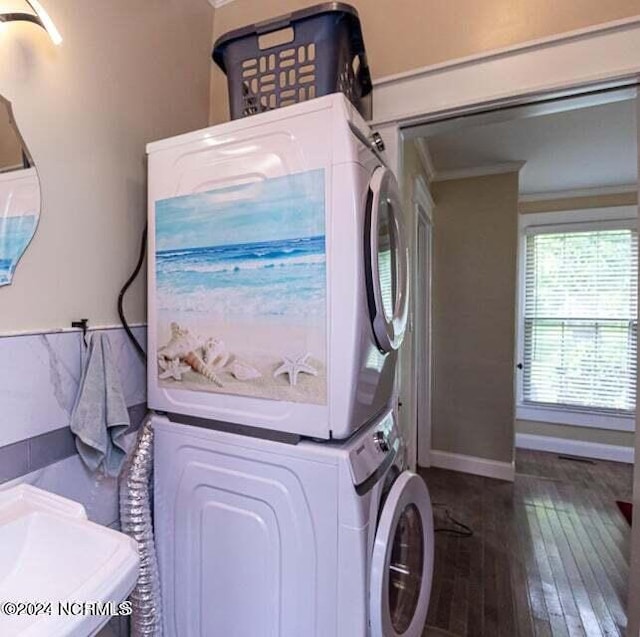 laundry area featuring laundry area, baseboards, hardwood / wood-style flooring, crown molding, and stacked washing maching and dryer