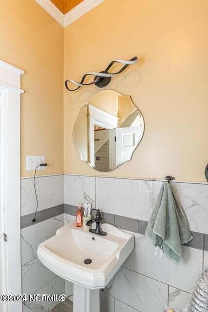 bathroom with a wainscoted wall, a sink, marble finish floor, crown molding, and tile walls