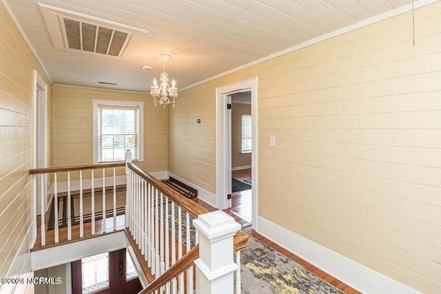 corridor with visible vents, wood finished floors, an inviting chandelier, crown molding, and an upstairs landing