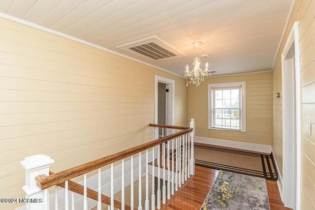 corridor with crown molding, visible vents, an inviting chandelier, an upstairs landing, and wood finished floors