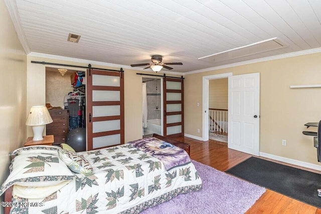 bedroom featuring a barn door, wood finished floors, attic access, and crown molding