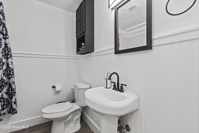 bathroom with visible vents, toilet, wainscoting, a sink, and wood finished floors