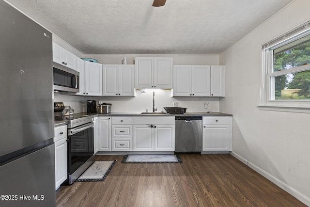 kitchen with dark wood-style floors, appliances with stainless steel finishes, a sink, and white cabinets