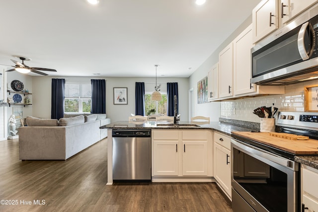 kitchen featuring tasteful backsplash, dark wood-style floors, appliances with stainless steel finishes, a peninsula, and a sink