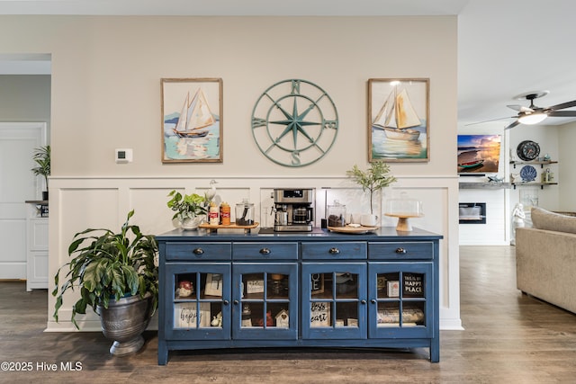 bar with dark wood-style floors, ceiling fan, a glass covered fireplace, and a decorative wall