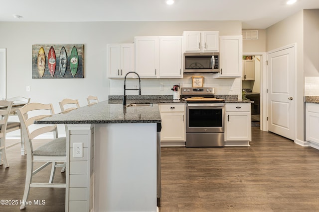 kitchen featuring a peninsula, a sink, visible vents, a kitchen breakfast bar, and appliances with stainless steel finishes