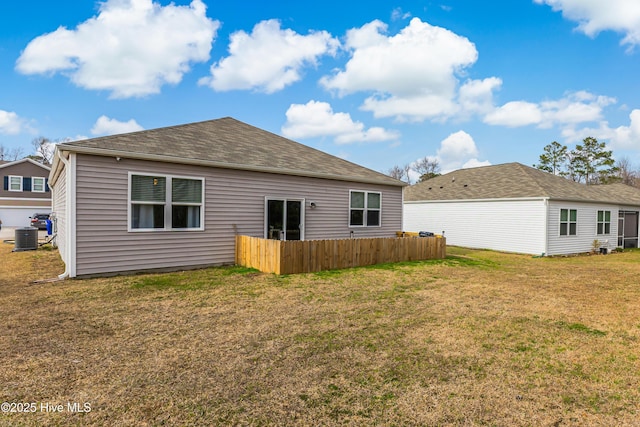 rear view of property with central AC unit, fence, and a lawn