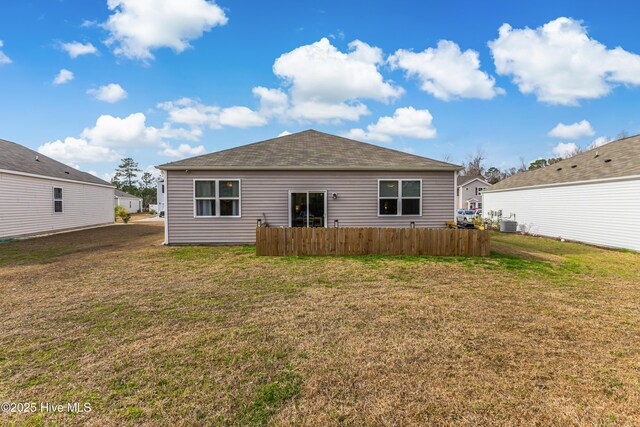 rear view of house featuring central air condition unit, fence, and a lawn