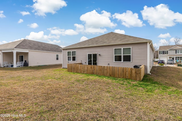 back of property with a lawn and fence