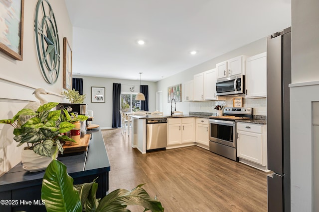 kitchen with wood finished floors, a peninsula, a sink, stainless steel appliances, and backsplash