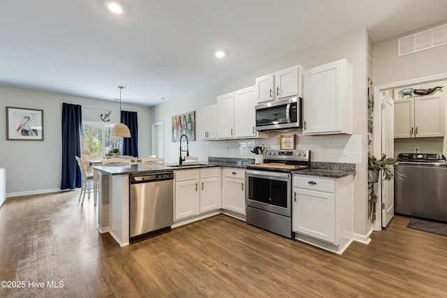 kitchen featuring dark wood-style floors, stainless steel appliances, a sink, washer / dryer, and a peninsula