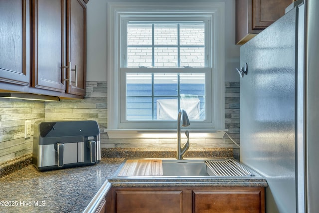 kitchen featuring dark countertops, backsplash, a sink, and freestanding refrigerator