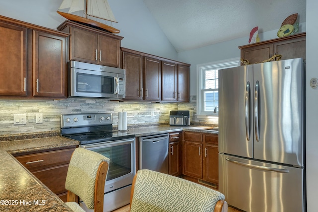 kitchen with stainless steel appliances, dark countertops, backsplash, vaulted ceiling, and a sink