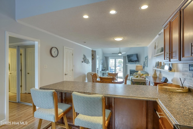 kitchen featuring light wood-style flooring, a peninsula, a fireplace, a ceiling fan, and ornamental molding