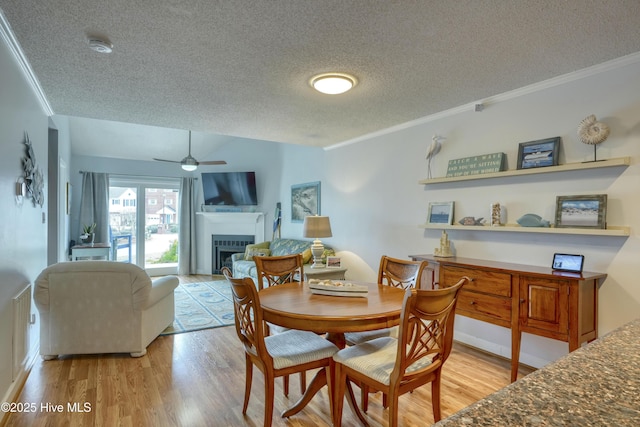 dining area featuring a fireplace, ornamental molding, a ceiling fan, a textured ceiling, and light wood-type flooring