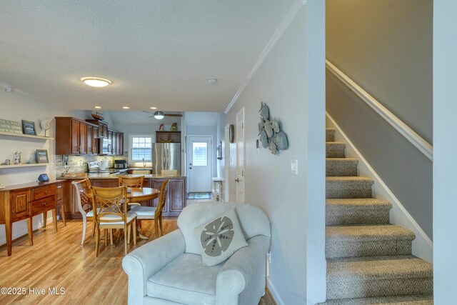 interior space with light wood finished floors, stairway, ornamental molding, a ceiling fan, and a textured ceiling