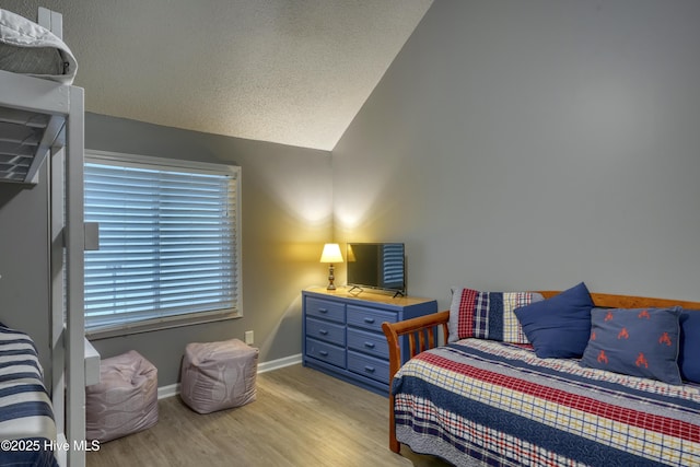 bedroom featuring baseboards, vaulted ceiling, light wood-style flooring, and a textured ceiling