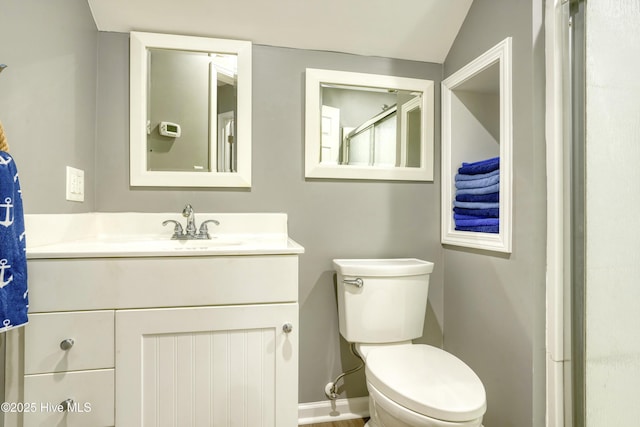 bathroom featuring baseboards, vaulted ceiling, vanity, and toilet