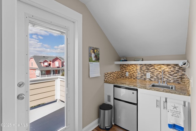 kitchen with vaulted ceiling, decorative backsplash, freestanding refrigerator, white cabinetry, and a sink