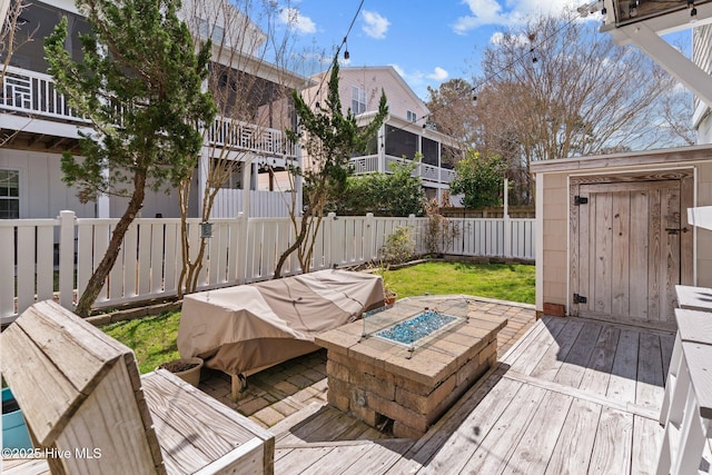 deck featuring a storage unit, an outbuilding, a fire pit, and a fenced backyard