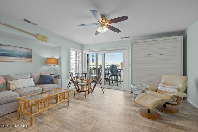 living room featuring light wood-type flooring, visible vents, and a ceiling fan