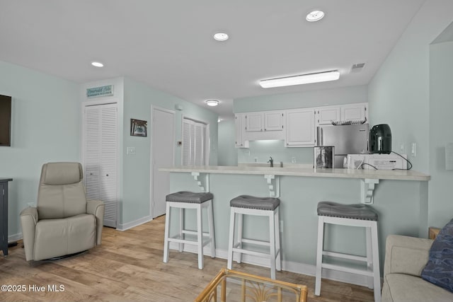 kitchen with white cabinets, a breakfast bar, light countertops, and freestanding refrigerator