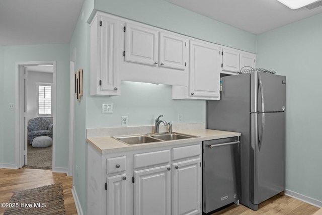 kitchen with stainless steel appliances, light countertops, a sink, and white cabinetry