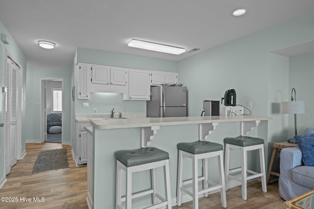 kitchen featuring a peninsula, white cabinetry, light countertops, freestanding refrigerator, and a kitchen bar