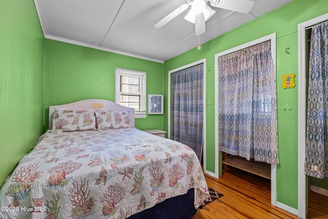 bedroom with wood finished floors, a ceiling fan, baseboards, multiple closets, and crown molding