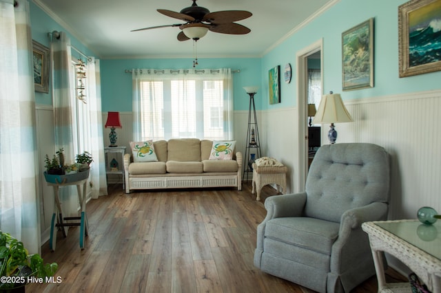 sitting room featuring a ceiling fan, crown molding, wood finished floors, and wainscoting