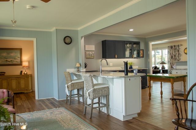 kitchen featuring crown molding, glass insert cabinets, light stone countertops, a peninsula, and a breakfast bar